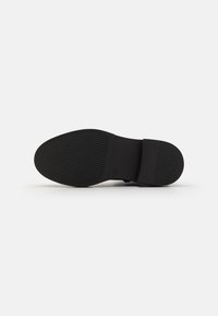 Talpa de pantof neagră cu un model texturat din cauciuc, oferind aderență. Dispune de o formă netedă, rotundă și un design minimalist.