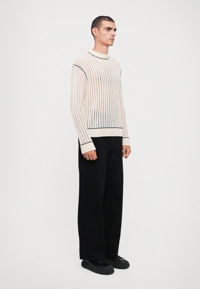 Light cream ribbed knit sweater with dark blue and black stripes, crew neckline, and long sleeves; paired with black wide-leg trousers.