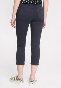 Pantalons capri ajustés bleu foncé avec une texture lisse, dotés de poches arrière et complétés par des baskets argentées brillantes.