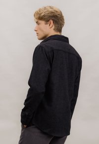 Svart flanellskjorte med lange ermer, knappeerm og spiss krage; har en teksturert stoff og buet hem.