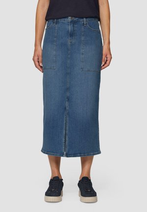 Jeansrock in Mittelblau mit geradem Schnitt. Hat zwei Vordertaschen, einen mittigen Schlitz und einen dezenten Saum. Kombiniert mit dunklen Sneakers.