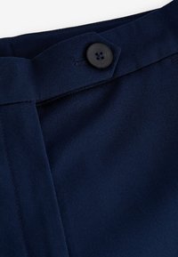 Tessuto blu navy con una texture liscia, caratterizzato da un unico bottone nero e cuciture curate vicino alla vita. Design classico, chiusura sartoriale.