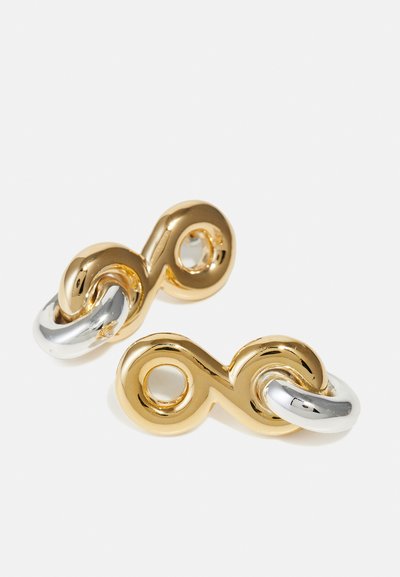 Boucles d'oreilles en métal doré et argenté présentant un motif de boucle d'infini entrelacée, avec une finition brillante et une texture lisse.