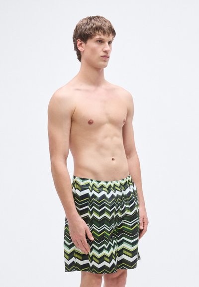 Πράσινα και μαύρα μαγιό σορτς με ζιγκ ζαγκ σχέδιο, ελαστική μέση και ελαφρύ υλικό, σχεδιασμένα να φτάνουν μέχρι το γόνατο.