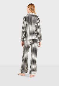 Zwart-wit gestreept pyjama-set met lange mouwen en broek. Voorzien van een kraag en manchetten met bredere strepen aan de zoom. Soepele stoftextuur.