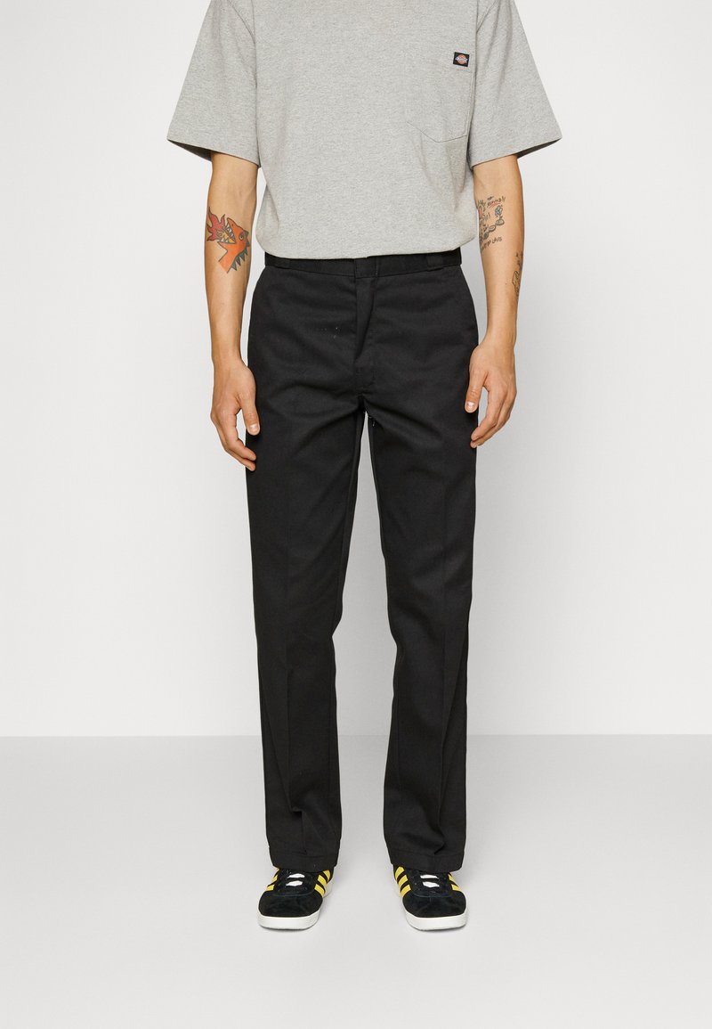 Black trousers with a straight fit, made of durable fabric; paired with a gray short-sleeve shirt and black/yellow sneakers.