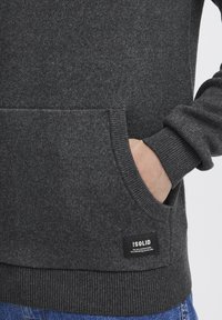 Dark gray knitted sweatshirt with a front pocket, ribbed cuffs, and a brand label on the lower edge. The fabric has a textured finish.