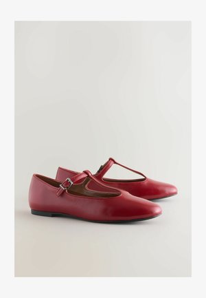 Ballerines en cuir rouge avec un design découpé et une bride de cheville, dotées d'un petit talon et d'une finition lisse, présentées sur un fond neutre.