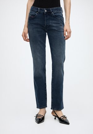 Personne portant un jean droit bleu foncé taille haute et des escarpins slingback noirs à bout pointu avec deux brides et petits nœuds.