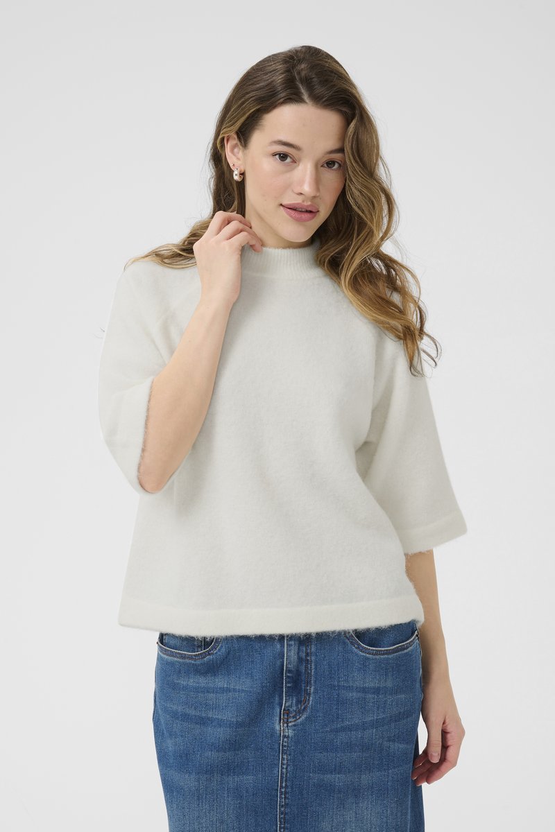 Suéter blanco, suave y de manga corta con un alto cuello, que presenta un corte holgado y un acabado texturizado. Combinado con una falda de denim.