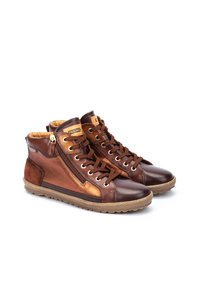Bottes chevilles en cuir marron avec une finition texturée, dotées d'une fermeture éclair sur le côté et d'un laçage à l'avant. Semelle en caoutchouc beige clair, design décontracté.