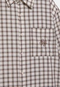 Beżowo-brązowa koszula w kratę na guziki z kieszenią na piersi, ozdobiona wyszywanym brązowym monogramem i kołnierzykiem.