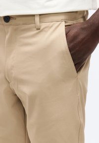 Κοντινό πλάνο ενός ατόμου που φοράει μπεζ παντελόνια με το χέρι χαλαρά τοποθετημένο στην μπροστινή τσέπη.