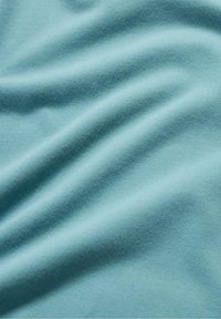 Ljus teal-tyg med en mjuk, slät textur, som har försiktiga vågor och veck. Materialet verkar lätt och något elastiskt.