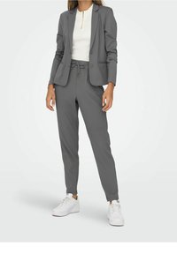 Grå skräddarsydd blazer med matchande joggerbyxor, slät tyg, figursydd design och elastisk midja, kombinerat med vita sneakers.