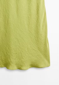 Hellgrünes Kleid aus strukturiertem Stoff, mit einem sanften Fall und einem geschwungenen Saum. Die Oberfläche hat ein leicht zerknittertes Aussehen.