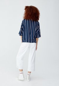 Chemise à rayures bleu marine avec manches amples, associée à un pantalon blanc court. Des baskets montantes blanches avec des accents rouges complètent la tenue.