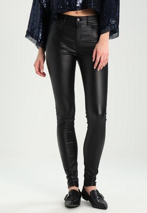 Sorte skinny jeans i imiteret læder med høj talje og en glat, skinnende overflade, stylet med en palietbesat cropped top og sorte loafers.