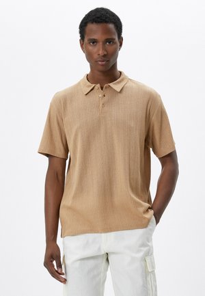 Tan ribbad polo-shirt med krage, tre-knappars placket och korta ärmar, tillsammans med ljusa cargobyxor.