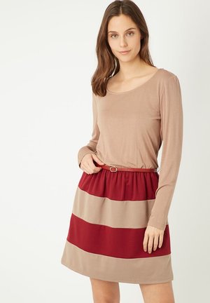 Top de manga larga en color beige, combinado con una falda a la altura de la rodilla con franjas horizontales alternas en beige y burdeos, ajustada en la cintura.