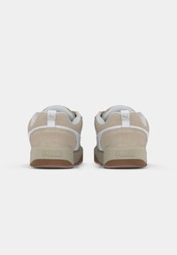 Beige zamšādas un baltas sieta sporta apavi ar noapaļotu pirkstu daļu, mīkstinātu apkaklīti un gumijas zoli, kurai ir izteikta Puma logo uz papēža.