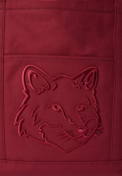 Vyšnių raudonos spalvos audinys su siuvinėtu lapės galvos dizainu. Yra struktūrinis siuvimas, suteikiantis reljefinį efektą. Paprastos, švarios linijos su aiškiai apibrėžtomis detalėmis.