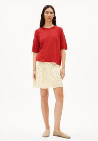 Rode textuur top met korte mouwen, gecombineerd met een crèmekleurige rok met uitsnijdingen. De outfit wordt afgemaakt met beige instapschoenen.