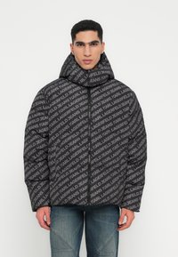 Juodas paminkštintas švarkas su pilku „KARL LAGERFELD JEANS“ raštu. Aukšta apykaklė, užtrauktukas priekyje ir laisvas siluetas. Tekstūruota medžiaga.
