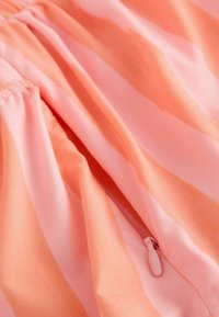 Gros plan d’un tissu soyeux pêche et rose avec couture froncée et détail du tire-zip assorti.