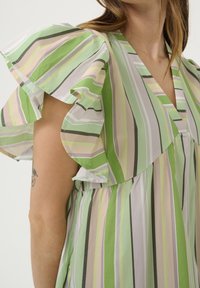 Lekkka, w paski sukienka w zielone, pastelowe i szare linie. Falbaniaste rękawy i fason w kształcie litery V, wykonana z miękkiego materiału.
