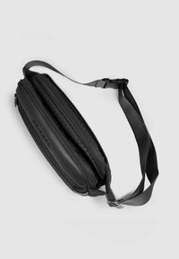 Bolso bandolera negro con un diseño elegante y acolchado. Cuenta con detalles texturizados, dos compartimentos con cremallera y una correa ajustable. Exterior suave.