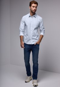 Vaaleansininen nappikauluspaita, jossa on rintatasku, yhdistettynä tummansinisiin farkkuihin ja beigen värisiin tennareihin. Asusteilla on rento leikkaus ja pehmeä tekstuuri.