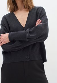 Mörkgrå cardigan med djup V-ringning, långa puffärmar och framknäppning. Mjuk textur och avslappnad passform. Minimalistisk design.