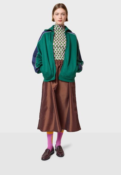 Zelena i mornarsko plava jakna na patentni zatvarač, uzorčani rolak, smeđi satenski suknja, ružičaste čarape i tamne mokasine sa dekorativnim šavovima.