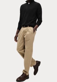 Schwarzer Zip-Kragen-Pullover, beigefarbene, gefaltete Hose und braune Schnürschuhe. Glattes Material mit lockerer Passform und klassischen Designelementen.