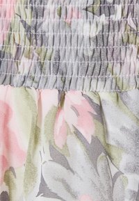 Blommönstrad tyg med rosa och gröna nyanser. Har en rynkad, texturerad smockdetalj upptill och en mjuk, lätt fall.