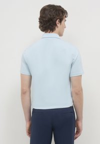 Polo shirt azzurro chiaro a maniche corte, tessuto morbido, colletto classico, vista posteriore con design minimale e dettagli di cucitura sottili, orlo arrotondato.