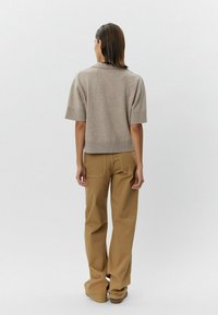 Krátky béžový pletený top s golierom, skombinovaný s voľnými pieskovými nohavicami. Oblečenie má neformálny, uvoľnený strih.