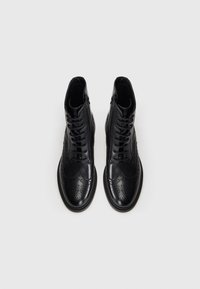 Black leather ankle boots with a smooth finish, brogue detailing, and matching laces. Angled toe and sturdy sole provide structure.