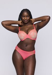 Korallinvärinen pehmustettu rintaliivi pitsiyksityiskohdalla ja säädettävillä olkaimilla, yhdistettynä vastaaviin bikinitaljoihin, joissa on pitsikoristeet vyötäröllä.