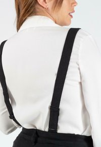 Chemise blanche à col avec des bretelles noires ajustables, présentant une texture lisse et un design minimaliste, mettant en valeur la zone des épaules.
