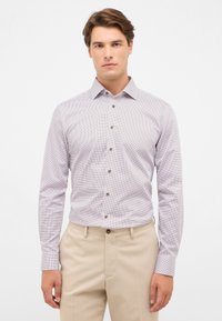 Witte shirt met kleine rode stippen, met bruine knopen, lange mouwen, met kraag, gecombineerd met beige broek. Gladde stoftextuur.