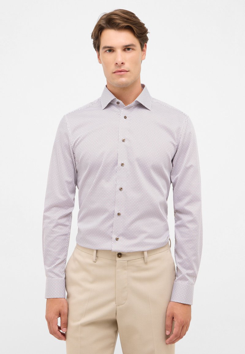 Witte shirt met kleine rode stippen, met bruine knopen, lange mouwen, met kraag, gecombineerd met beige broek. Gladde stoftextuur.