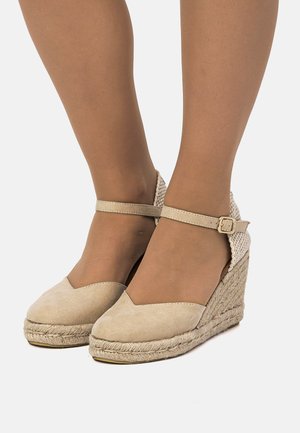 Sandales compensées espadrilles beiges avec une tige en daim, un design d'orteil en forme de V et un talon tissé. Bride de cheville réglable avec un détail boucle en métal.