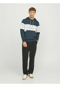 Blå og hvid farveblokket hoodie med et frontlogo, snoretræk i hætten og ribbede manchetter, parret med sorte plisserede bukser og hvide sneakers.