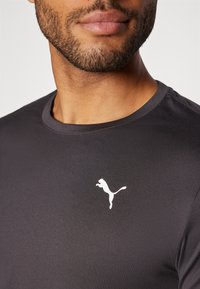 Čierne športové tričko s okrúhlym výstrihom, na hrudi je malé biele logo Puma. Hladká tkanina s jemným leskom.