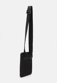 Sac bandoulière noir fabriqué en tissu durable, avec une fermeture à glissière, une sangle réglable et une forme rectangulaire épurée au design minimaliste.