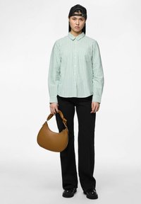 Lichtgroen en wit gestreept overhemd met knopen, zwarte wijde broek, en een bruine kromme handtas met een gestructureerd oppervlak en stevige handgreep.