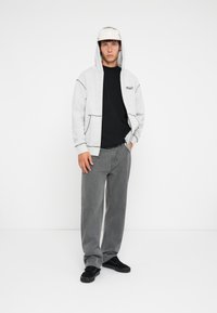 Grå hettegenser med frontlomme, kombinert med en svart t-skjorte og grå straight-leg jeans. Svarte sneakers fullfører antrekket. Lys caps på hodet.