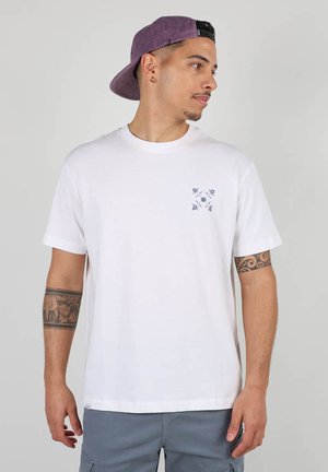 T-shirt blanc à manches courtes avec un design géométrique bleu sur la poitrine gauche. Tissu en coton ; il présente un col rond et une coupe décontractée.